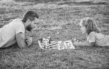 Mutlu bir ebeveyn ve oğul ailesi parkta yeşil çimlerde satranç oynuyor, satranç oynuyor..