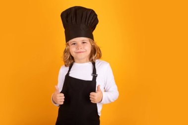 Cooking children. Chef kid boy in form of cook. Child boy with apron and chef hat preparing a healthy meal on studio isolated background. Cooking process