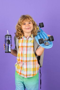Mavi arka plan üzerinde kaykay ve su şişesi tutan mutlu çocuk izole edildi. Moda çocuklarının resim stüdyosu