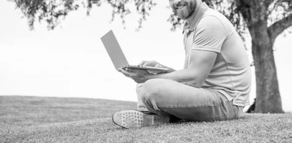 cropped smiling guy check email. freelance man post blog online sit on grass. writing online. businessman using laptop for blogging. social network and weblog. modern business computer communication.