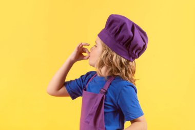 Kid in cooker uniform and chef hat preparing food on studio color background. Cooking, culinary and kids food concept