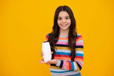 Teen child girl with shampoo bottle or shower gel isolated on yellow background. Kids hair cosmetic product. Happy teenager, positive and smiling emotions of teen girl
