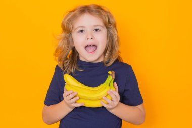 Çocuklar için vitamin ve sağlıklı meyveler. Çocuk stüdyoda muz tutuyor. Sarı arka planda muzları olan şirin bir çocuğun stüdyo portresi, boşluğu kopyala