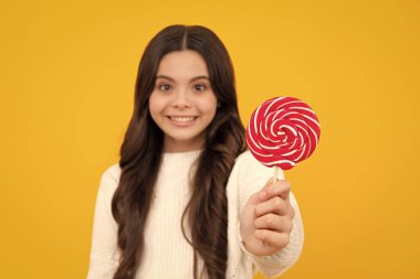 Genç kız sarı arka planda lolipop karamel tutuyor, şekerci dükkanı. Tatlılı ergen enayiler. Mutlu yüz, pozitif ve gülümseyen genç kız duyguları