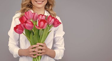 positive blond woman with spring tulip flowers on grey background.