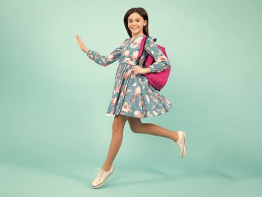 Okul üniformalı, sırt çantalı bir kız. Mavi soyutlanmış genç bir kız öğrenci. Öğrenme ve eğitim çocukları. Koş ve atla. Mutlu ergen, pozitif ve gülümseyen duygular