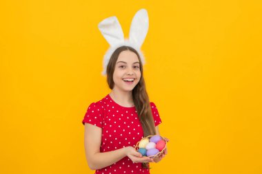 Paskalya çocuk bayramı konsepti. Mutlu, gülümseyen, tavşan kulaklı bir genç kız elinde boyalı paskalya yumurtaları