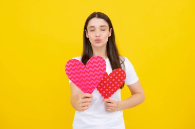 Sarı arka planda elinde kağıt kalple gülümseyen güzel bir kadının portresi. Aşk konsepti. Mutlu kadınlar için aşk sembolleri, sevgililer günü ya da doğum günü