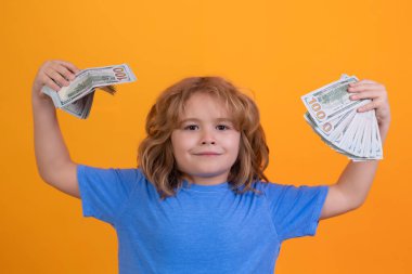 Child with lots of money dollar banknotes isolated over yellow studio background