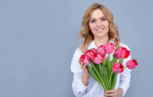 stock image smiling young woman with spring tulip bouquet on grey background.