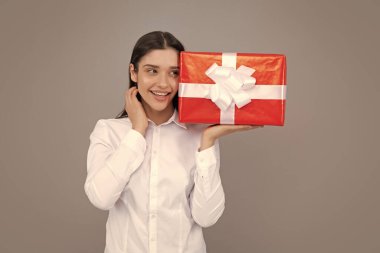 Mutlu gülümseyen bir kızın portresi hediye kutusunu tutuyor ve gri arka planda izole edilmiş.