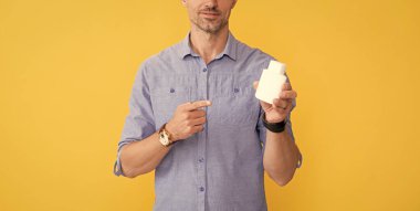 Kırpılmış adam sarı arka planda vitamin şişesi gösteriyor, sağlık.
