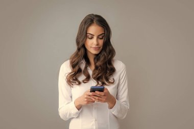 Akıllı telefonu olan ciddi bir kadın. Cep telefonu olan genç bir kadın. Gri arka planda akıllı telefonu olan bir iş kadını