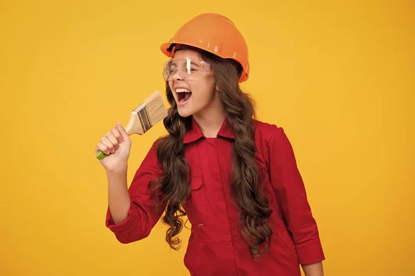 stock image Excited teenager builder expert in helmet on construction site. Teen girl painter with painting brush tool or paint roller. Child on repairing work. Renovation concept