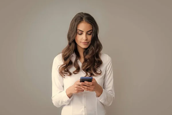一个带着智能手机的严肃女人一个拿着手机的年轻女人拥有灰色背景智能手机的女商人 — 图库照片