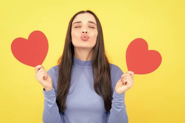 Aşkı hisseden bir kız. Sarı arka planda elinde kağıt kalple gülümseyen güzel bir kadının portresi. Aşk konsepti