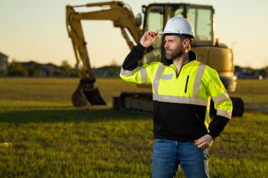 İnşaat alanında çalışan bir işçi. Şapkalı bir inşaatçı. Kasklı bir inşaat işçisi. Miğferli inşaat işçisi. İnşaat binasında sanayi işçisi. İnşaatçı, kazıcıyla birlikte inşaat alanında.