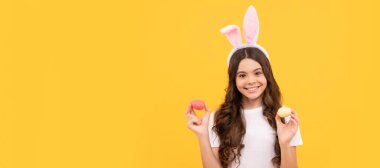 Tavşan kulaklı mutlu çocuk sarı arka planda yumurta tutuyor. Paskalya çocuğu yatay posteri. Tavşan çocuğun web afişi, kopyalama alanı