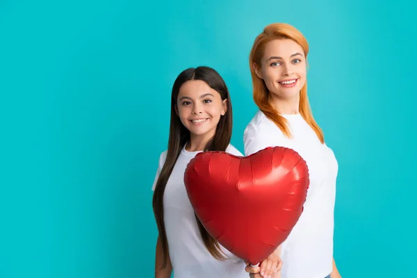 Love mom. Mother and daughter hold heart balloon. Happy mother and daughter holding love heart balloon on blue background