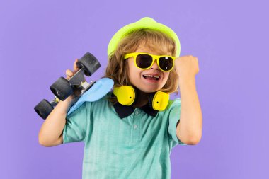 Violet 'in arka planında uzun tahta tutan çocuk. Pennyboard 'u olan çocuk. Moda şapkalı ve güneş gözlüklü neşeli küçük çocuğun stüdyo fotoğrafı.