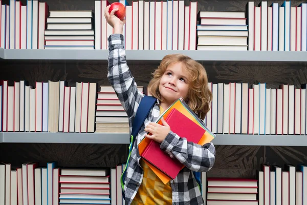 図書館で本とリンゴを持つ学校の少年 学校の子供は授業で学び 学校で英語を勉強します 小学生 面白い弟子学習の肖像画 — ストック写真