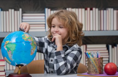 School kid pupil looking at globe in library at the elementary school. World globe. School kid 7-8 years old with book go back to school. Little student. Education concept