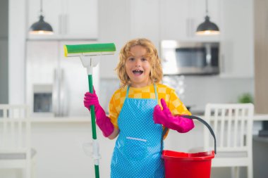 Portrait of child cleaning, concept growth, development, family relationships. Housekeeping and home cleaning concept. Child use duster and gloves for cleaning. Home kitchen background