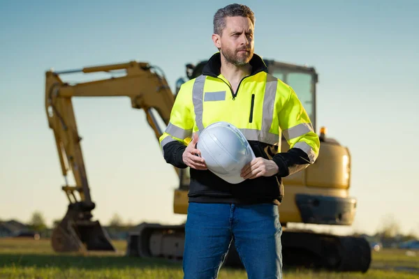 Portrait of builder in a construction site. Builder with excavator ready to build new house. Construction builder wear building uniform on excavation truck digging, builder construction