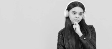 thinking child in headphones on yellow background. Child portrait with headphones, horizontal poster. Girl listening to music, banner with copy space