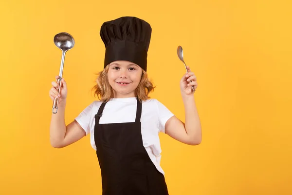 stock image Funny kid chef cook with kitchen ladle and spoon, studio portrait. Chef kid boy making healthy food. Portrait of little child in chef hat isolated on studio background. Child chef. Cooking process