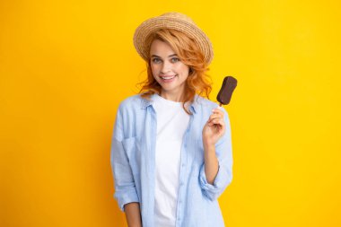 Genç bir kadının nefis dondurma yediği, dondurulmuş tatlıdan hoşlandığı, günlük kıyafetler giydiği, sarı arka planda izole edilmiş bir fotoğraf.