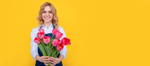 黄色の背景に春のチューリップの花とエプロンの幸せな花の売り手の女性 女性隔離された顔の肖像画 モックアップ付きバナーコピースペース — ストック写真