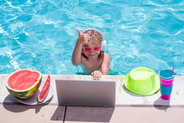 Child working with laptop on summer vacation holidays. Little freelancer using computer, remote working in swimming pool. Summer online technology