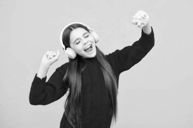 Teenager child girl in headphones listening music, wearing stylish casual outfit isolated over yellow background