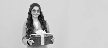 Güneş gözlüklü ve takım elbiseli neşeli çocuk sarı arka planda hediye kutusu tutuyor, alışveriş yapıyor. Yetenekli çocuk, yatay poster. Kopyalama alanı olan başlık