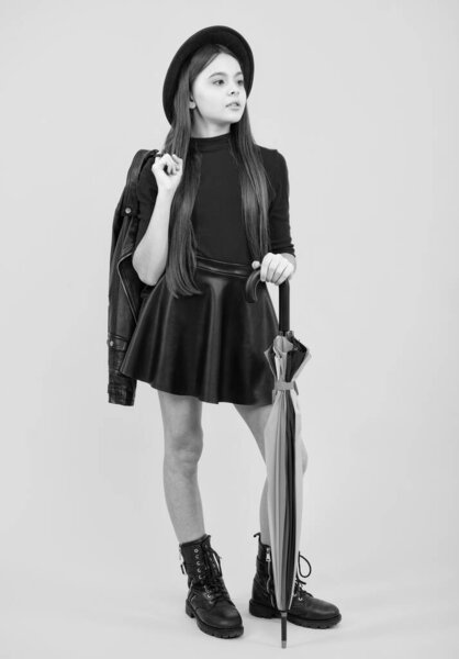 Fashion autumn kids weather. Child teenager girl with umbrella in autumn black leather skirt boots and hat isolated on yellow studio background. Fall fashion accessory. Autumn trendy clothes