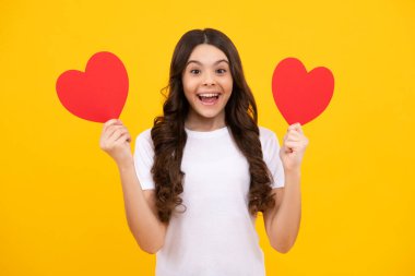 Cheerful lovely romantic teen girl hold red heart symbol of love for valentines day isolated on yellow background. Happy teenager, positive and smiling emotions of teen girl