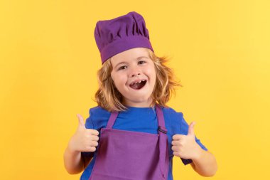 Komik çocuk şef stüdyo portresi yapıyor. Çocuk aşçı, izole stüdyo geçmişinde yemek hazırlıyor. Çocuklar yemek yapıyor. Önlüğü ve aşçı şapkası olan genç çocuk sağlıklı bir yemek hazırlıyor.