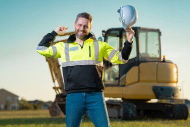 İnşaat alanındaki bir inşaatçının portresi. Kazıcı yeni bir ev inşa etmeye hazır. İnşaat işçileri kazı kamyonu kazılarında inşaat üniforması giyerler, inşaat işlerinde çalışırlar.