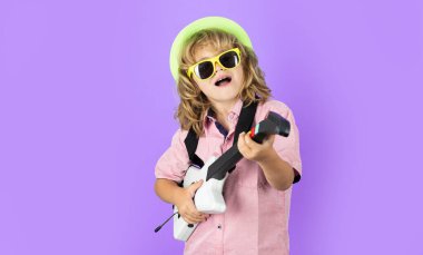 Pembe güneş gözlüklü, elektro gitar çalan küçük çocuğun portresi. Sevimli çocuk parlak duygularla elektro gitarla şarkı söyler ve çalar.