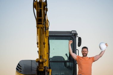 Portrait of worker man small business owner. Construction worker with hardhat helmet on construction site. Construction engineer worker in builder uniform with excavation truck digging. Worker