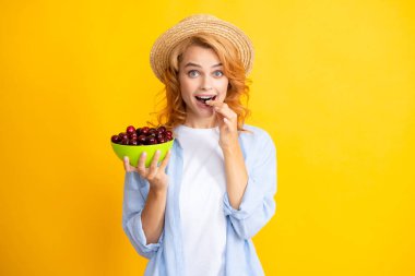 Kiraz meyvesi topluyorum. Genç bir kadın tatlı kiraz yiyor. Sarı arka planda kirazlı güzel bir kızın portresi. Yaz meyve toplama mevsimi. Doğal vitaminler