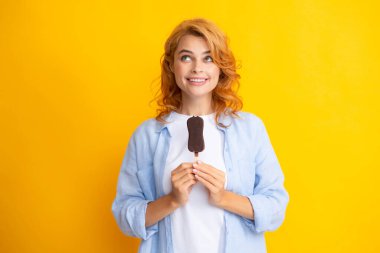 Neşeli, komik genç kızın portresi soğuk dondurulmuş tatlı yemekten, lezzetli çikolatalı dondurma yemekten, sarı arka plandan hoşlanıyor.