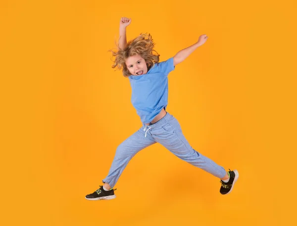 Kid boy jump fly movement wear shirt and jeans isolated on yellow studio background