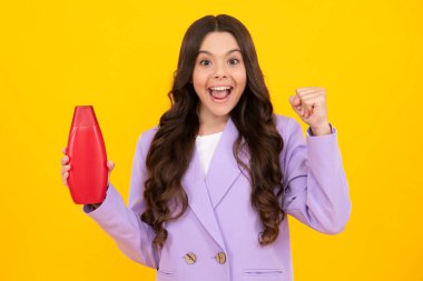 Teen child girl with shampoo bottle or shower gel isolated on yellow background. Kids hair cosmetic product. Happy teenager, positive and smiling emotions of teen girl