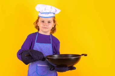 Çocuk aşçı tavayla yemek pişirir. Çocuk fırın üniforması ve aşçı şapkası giyiyor yemek hazırlıyor, stüdyo fotoğrafı çekiyor.