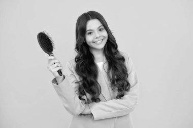 Teenager brushing combing hair with big comb on yellow isolated studio background. Teen girl with hairbrush. Kids hairstyle. Happy positive and smiling emotions of teenager girl