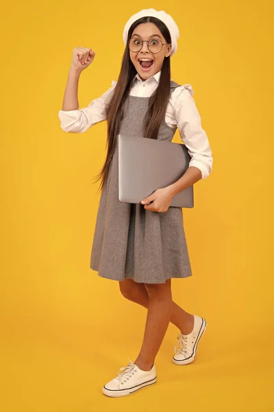 Excited face. Smart little boy with laptop in casual clothes isolated over yellow background. Excited teenager school girl