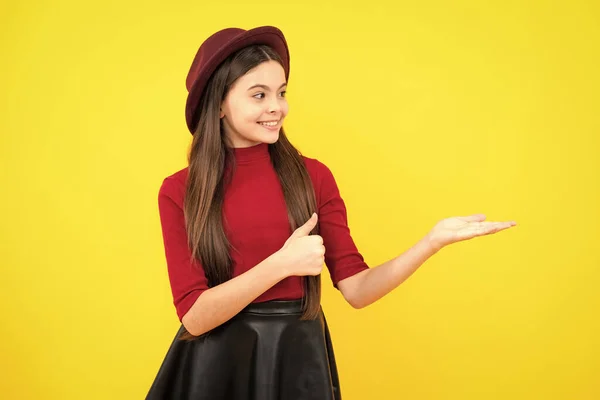 Look at advert. Teenager child points aside shows blank copy space for text promo idea presentation, poses against yellow background. Happy teenager portrait. Smiling girl