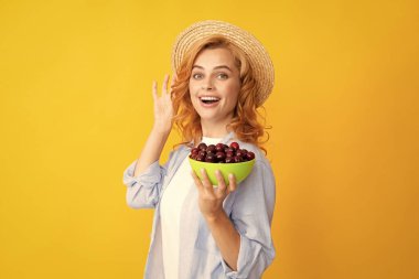 Çekici genç bir kadın taze kiraz yiyor. Sağlıklı yaz meyveleri. Sarı arka plan. Kirazla poz veren güzel bir kadın, kirazlı bir kız...